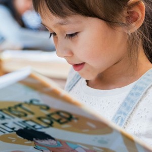 Dívka, která soustředěně čte a dívá se do otevřené, anglické dětské knihy.