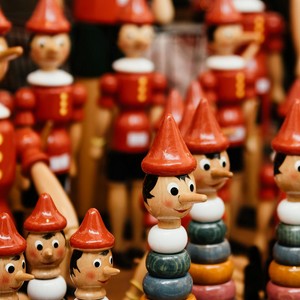 Dřevěné figurky Pinocchia s dlouhými nosy a červenými čepicemi. Symbol nejznámější italské pohádky.