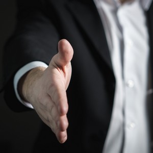 Detailní záběr na pravou ruku muže v černém saku a bílé košili, která je natažená k podání ruky.