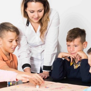 Lektorka angličtiny sleduje skupinu dětí, které hrají deskovou hru s kostkou.