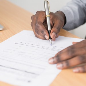 Muž se stříbrným plnicím perem podepisuje dokument ležící na dřevěném stole.