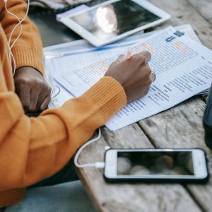 Člověk telefonuje v angličtině se sluchátky v uších a poznámkami před sebou.