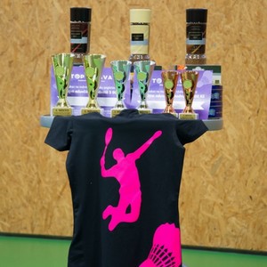 Stojan s poháry pro vítěze badmintonového turnaje a černé tričko s růžovou siluetou badmintonisty.
