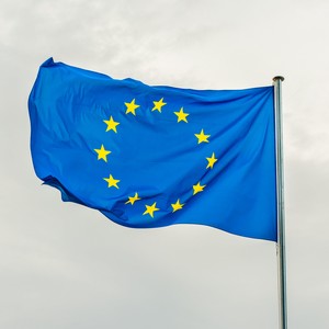 Vlajka Evropské unie vlající na stožáru pod zataženou oblohou