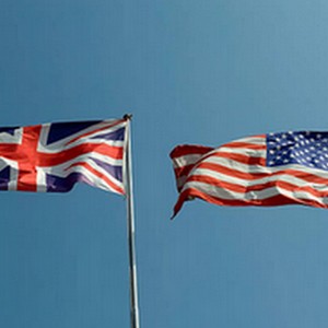 Dvě vlajky vlající na stožárech proti jasně modré obloze: britská vlajka a vlajka Spojených států amerických.