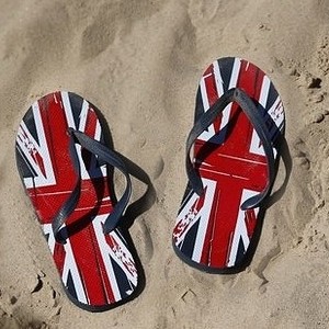 Letní žabky s motivem britské vlajky ležící na písku.