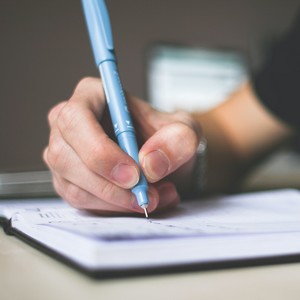 Muž, který píše do otevřeného poznámkového bloku s kroužkovou vazbou.