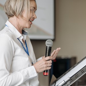 Usmívající se žena mluví do mikrofonu při tlumočení nebo prezentaci.